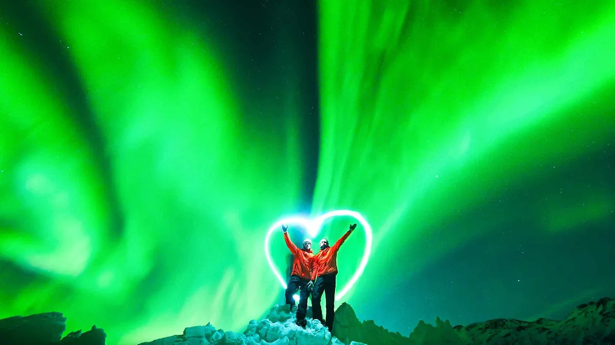 Minibus parked on a snowy roadside under a green aurora arc on a Tromso aurora borealis tour, Troms, northern Norway
