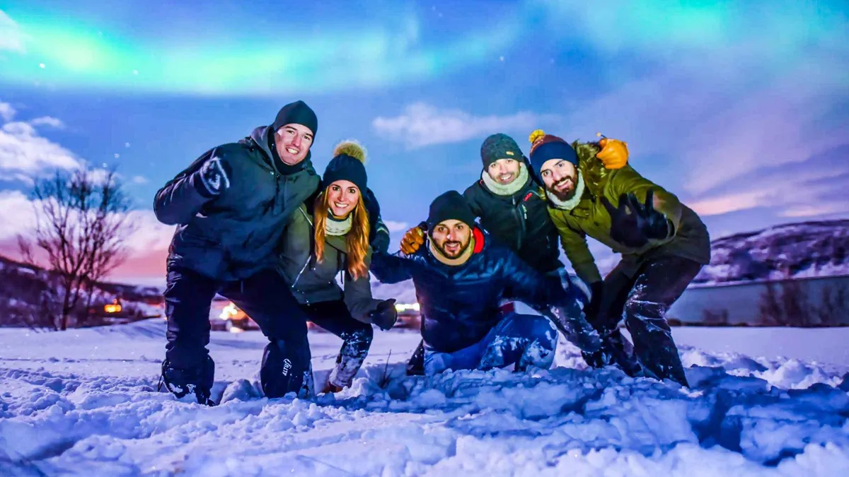 Small group around a campfire in thermal suits watching the aurora on a premium Tromso aurora borealis tour in Troms, Norway